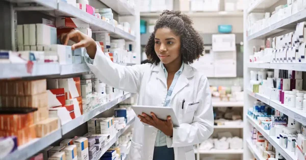 A young pharmacy resident sorts medications while holding a notepad.